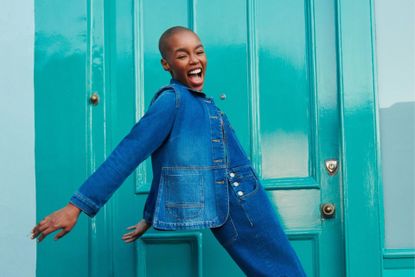 Woman dressed in White Stuff denim jacket and jeans standing in front of a bright coloured door