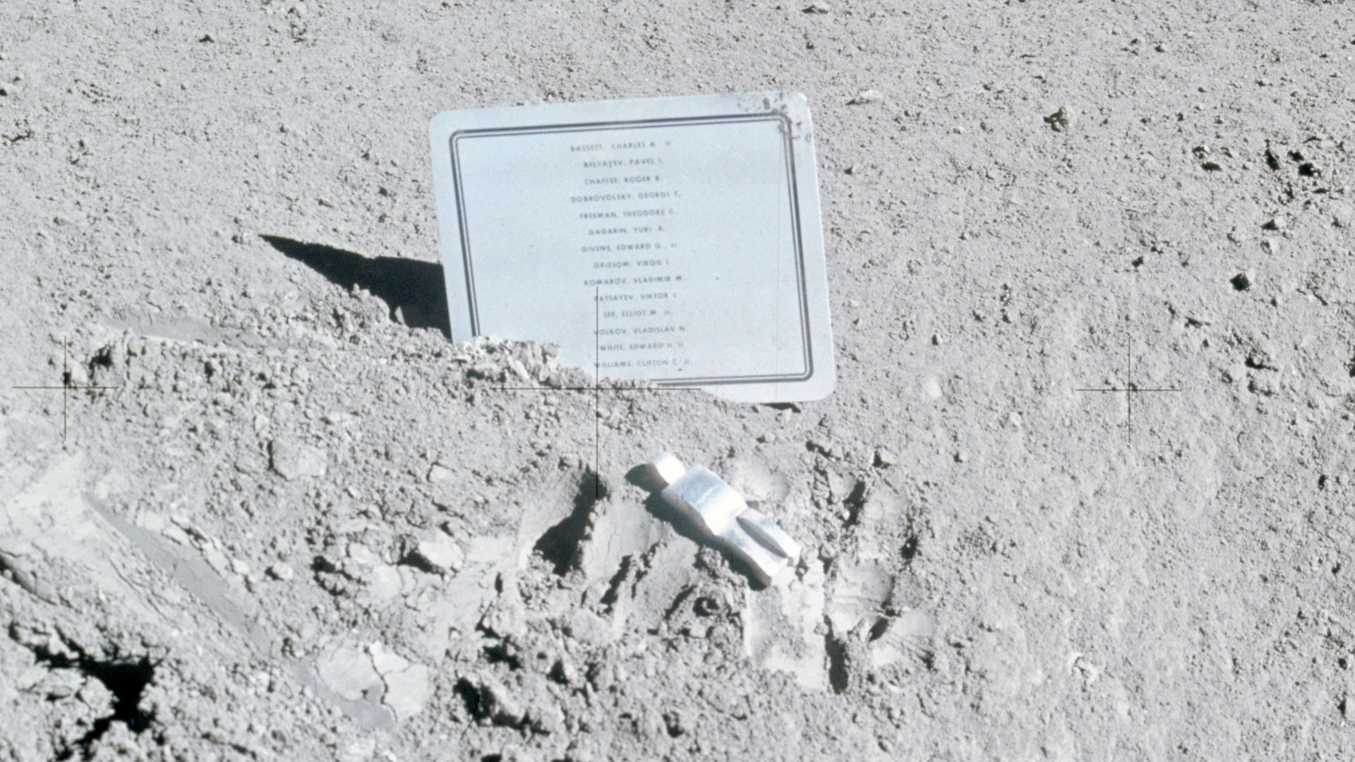 a plaque and aluminum figure lie on the surface of the moon