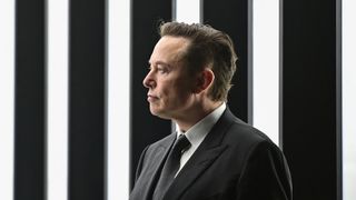 Et bilde av Elon Musk i dress, mot sorte og hvite vertikale striper