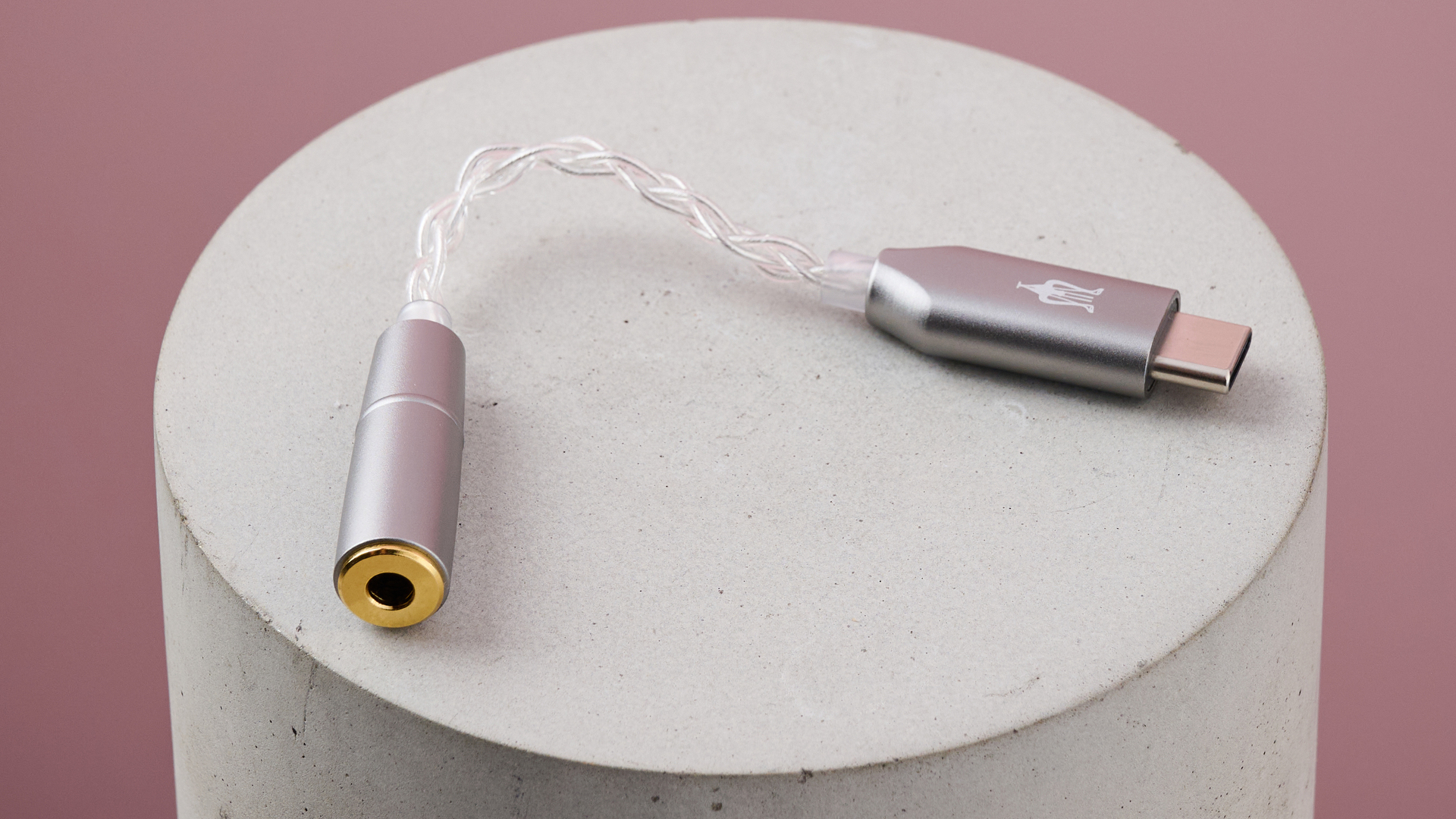 Meze Audio Alba&#039;s USB-C adapter on circular surface against a pink background