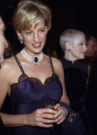 A headshot of Princess Diana at the Met Gala 1996, showing her navy silk slip dress and sapphire and diamond jewellery