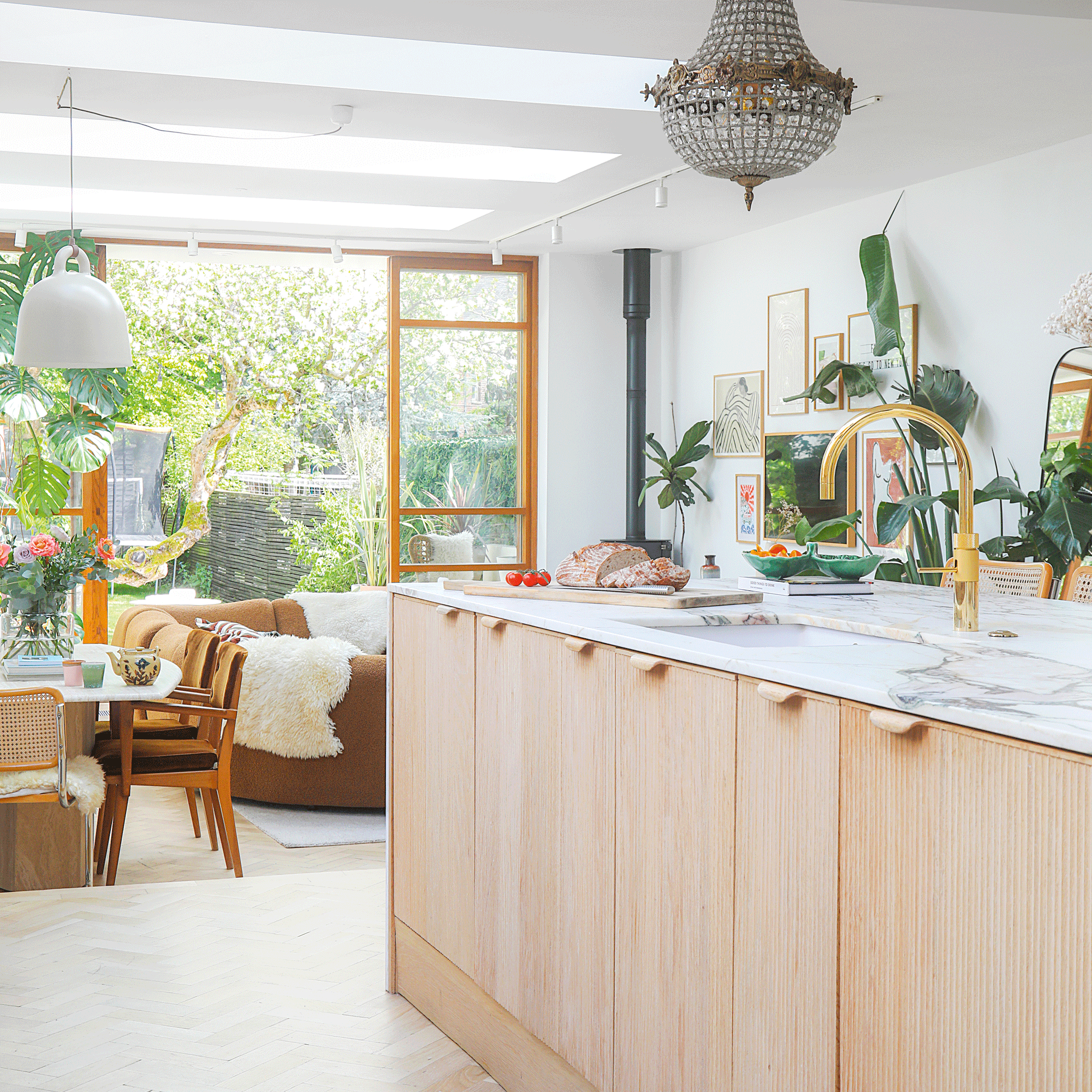 an open plan space with a marble topped kitchen island leading into dining area with table and chairs and a living area with sofas which leads out into a garden via bifold doors