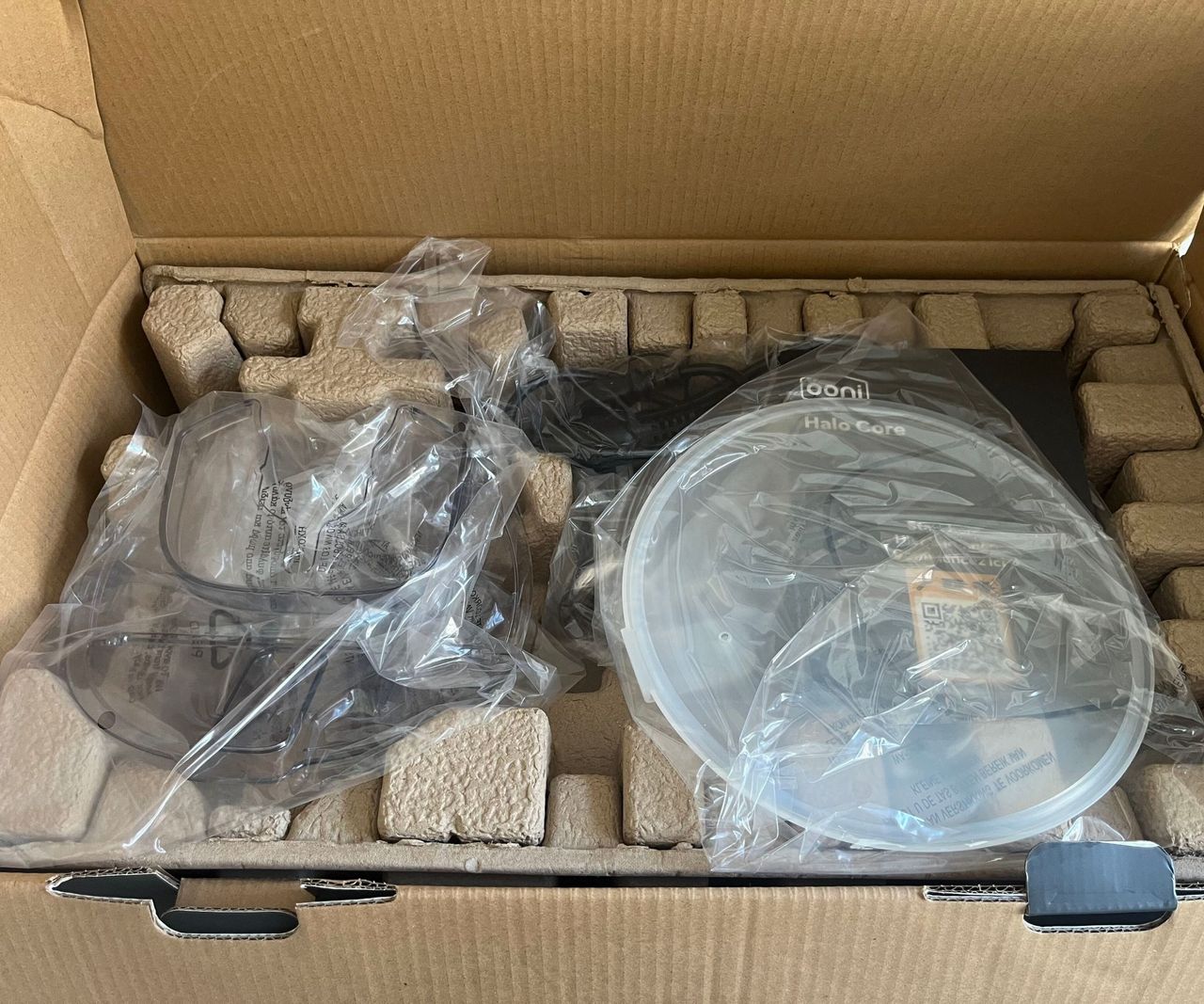 Accessories for a stand mixer in plastic bags nestled on a piece of cardboard