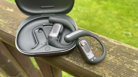 Shokz Openfit Pro outside, outside held in a woman's hand, with green grass in the background