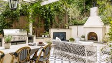 An outdoor kitchen, dining, and living area with warm neutral walls, patterned concrete floor tiles, a large fireplace, a stainless steel stove, and a large rectangular dining table