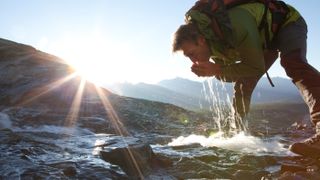 Hiker drinks from mountain stream at sunrise