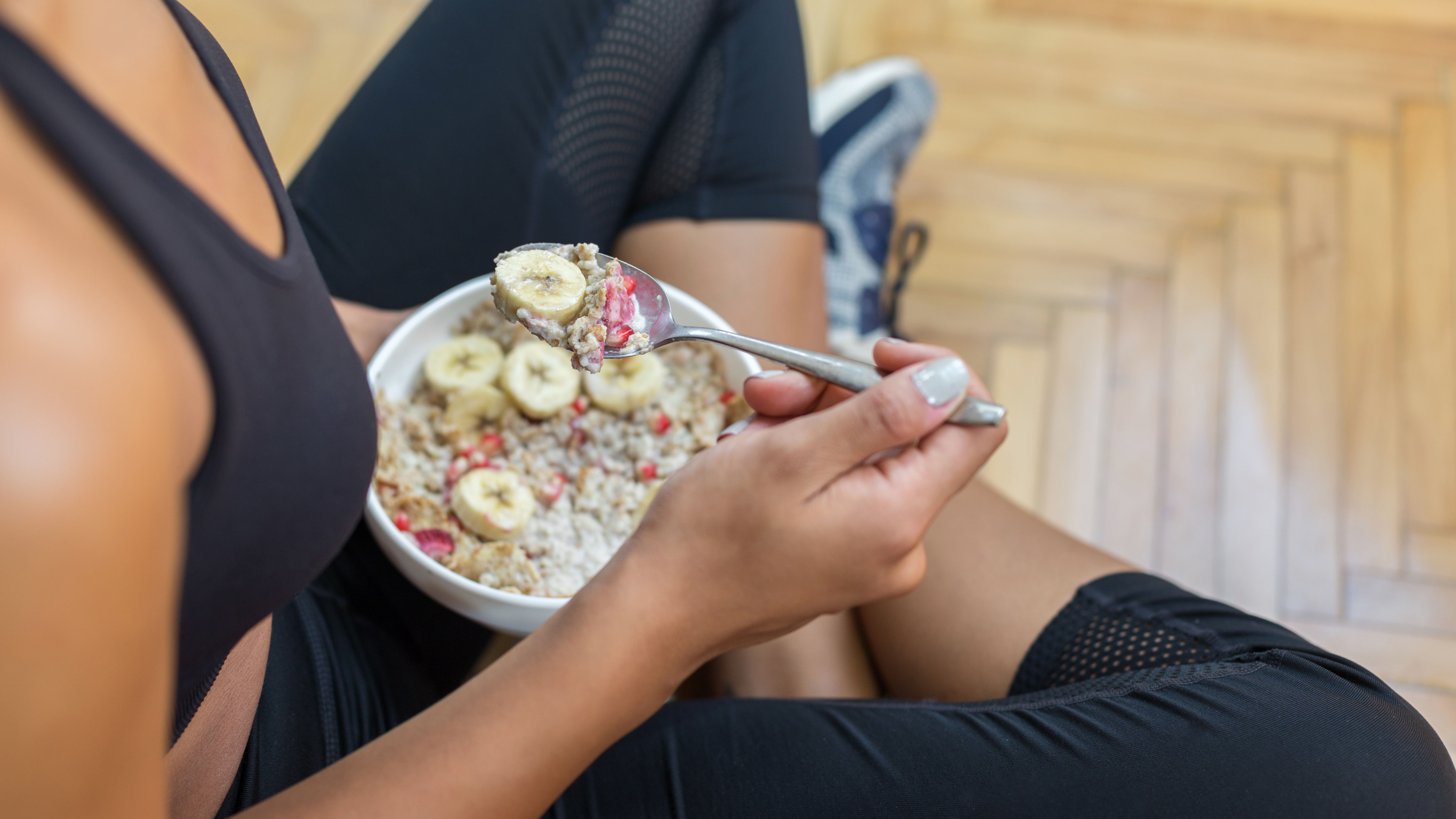 Mujer con ropa de entrenamiento comiendo avena y fruta