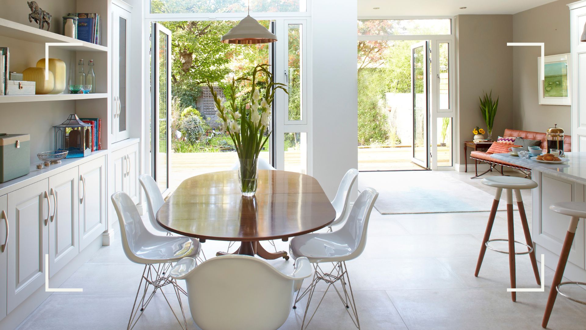 open plan kitchen dining area in neutral colours with two sets of French doors open to a garden 