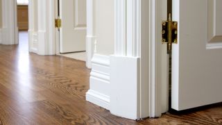 Close up of white decorative skirting boards next to a dark wooden floor