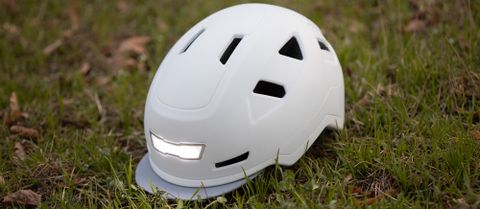 A white Xnito e-bike helmet sits on grass, with the front light illuminated