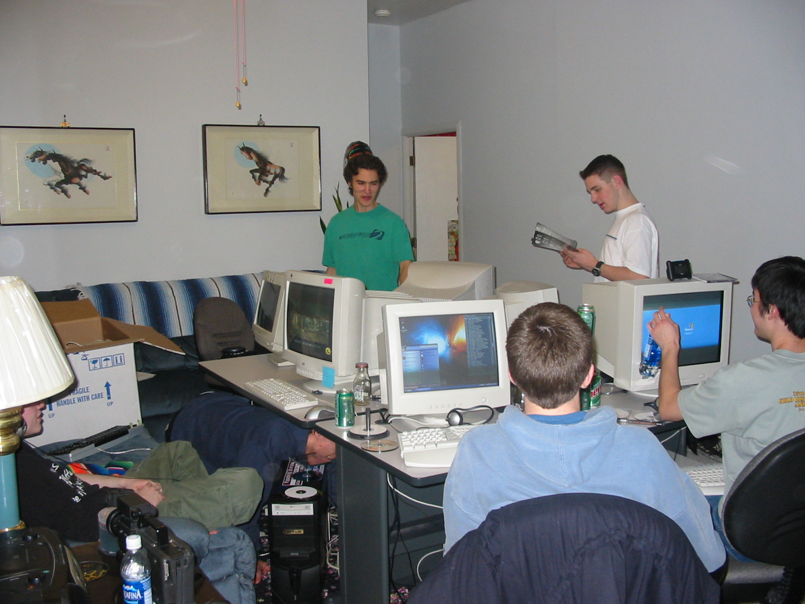 A group of gamers surround a table covered with CRT monitors in large room.