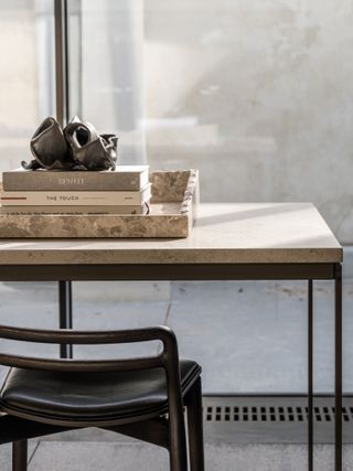 A detail of the extended countertop area with a bar chair next to the floor-to-ceiling windows. On the countertop, there is a tray made of stone with books on it.