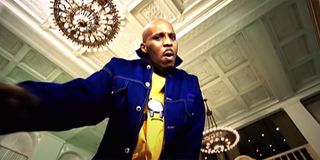 DMX with a yellow shirt on and a white coat inside a bank rapping.