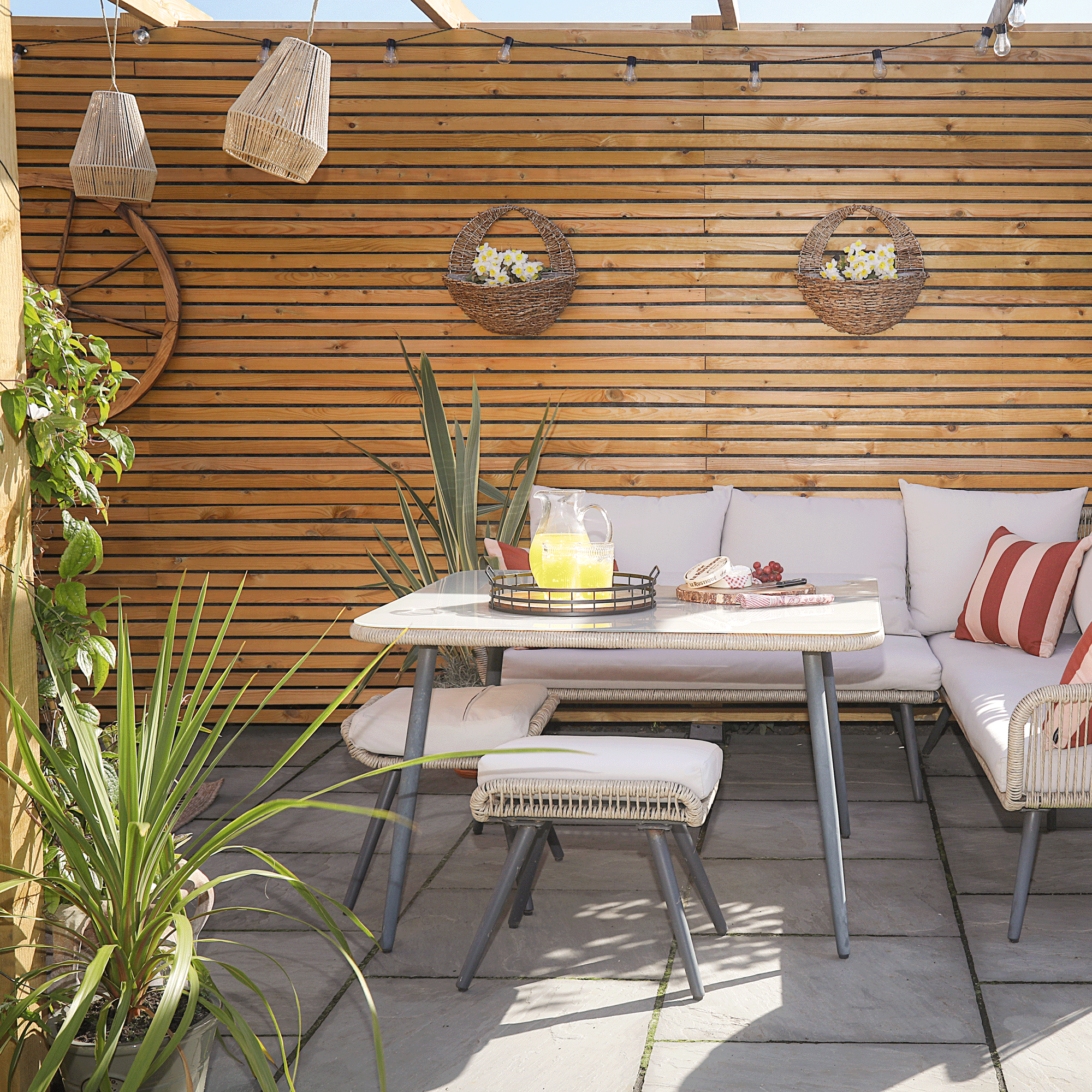 a patio area with a pergola and horizontal fencing with a corner outdoor sofa and hanging baskets
