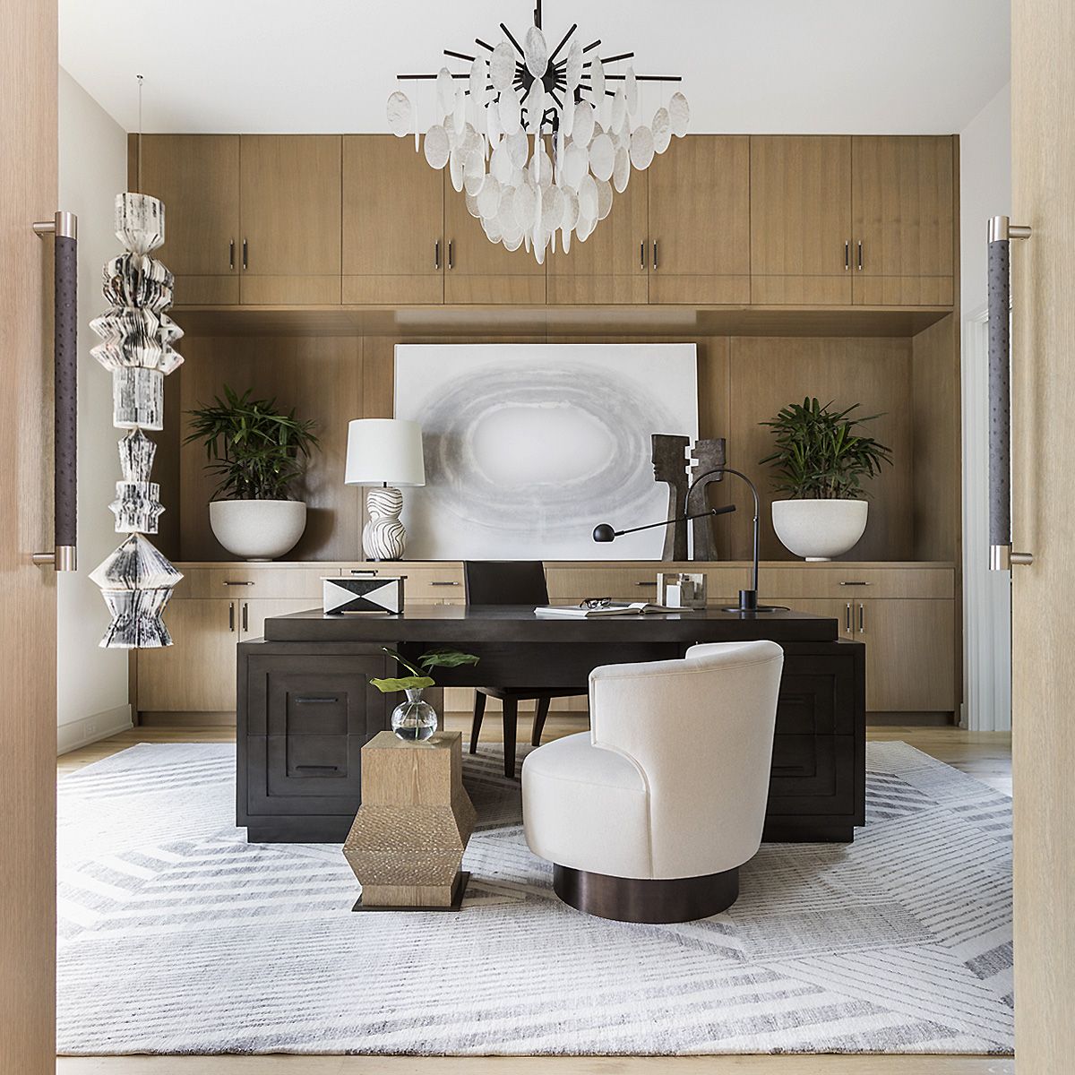 Home office with dark desk, desk chair and armchair, built-in cabinetry, pendant light, desk lamp and table lamp