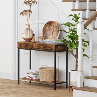 a wooden entryway console table two oversized plants on and near it,and a wooden staircase to the right