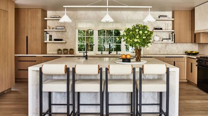 A neutral Los Angeles kitchen with wooden cabinets, a marble island and white light fixtures