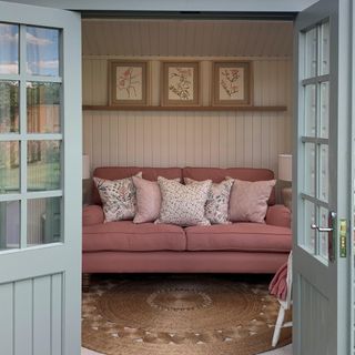 A garden office with a seating area featuring a pink sofa with floral scatter cushions