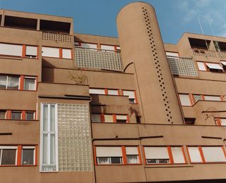 A housing complex in brown concrete with red window frames, glass blocks and balconies