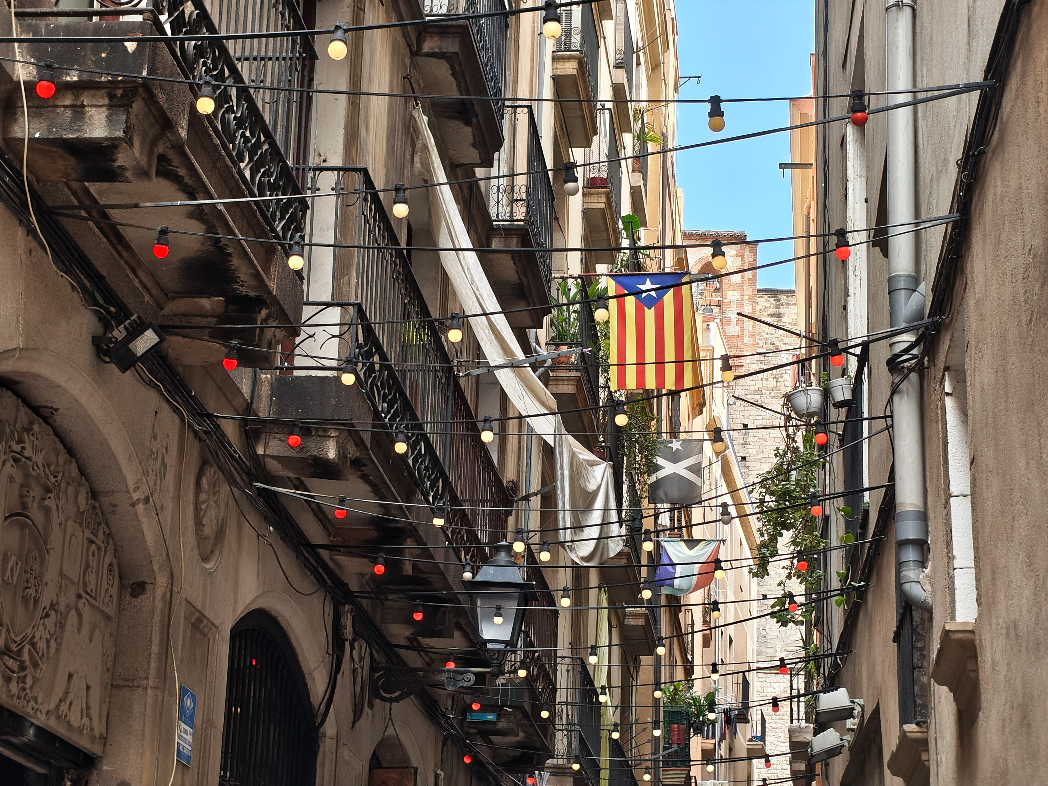 Narrow European street lined with balconies and criss-crossing festoon lights, with a Catalan flag hanging from a building, photographed with the Nothing Phone (4a).