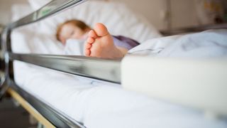 young girl pictured lying in a hospital bed, her face is blurred out