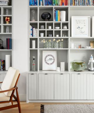 inbuilt storage cupboards and shelves in pale grey with books and ornaments beside wooden flooring and a grey rug.