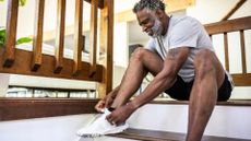 man sitting on an indoor step tying up shoes laces on his trainers, dressed in a tshirt and shorts ready for a run