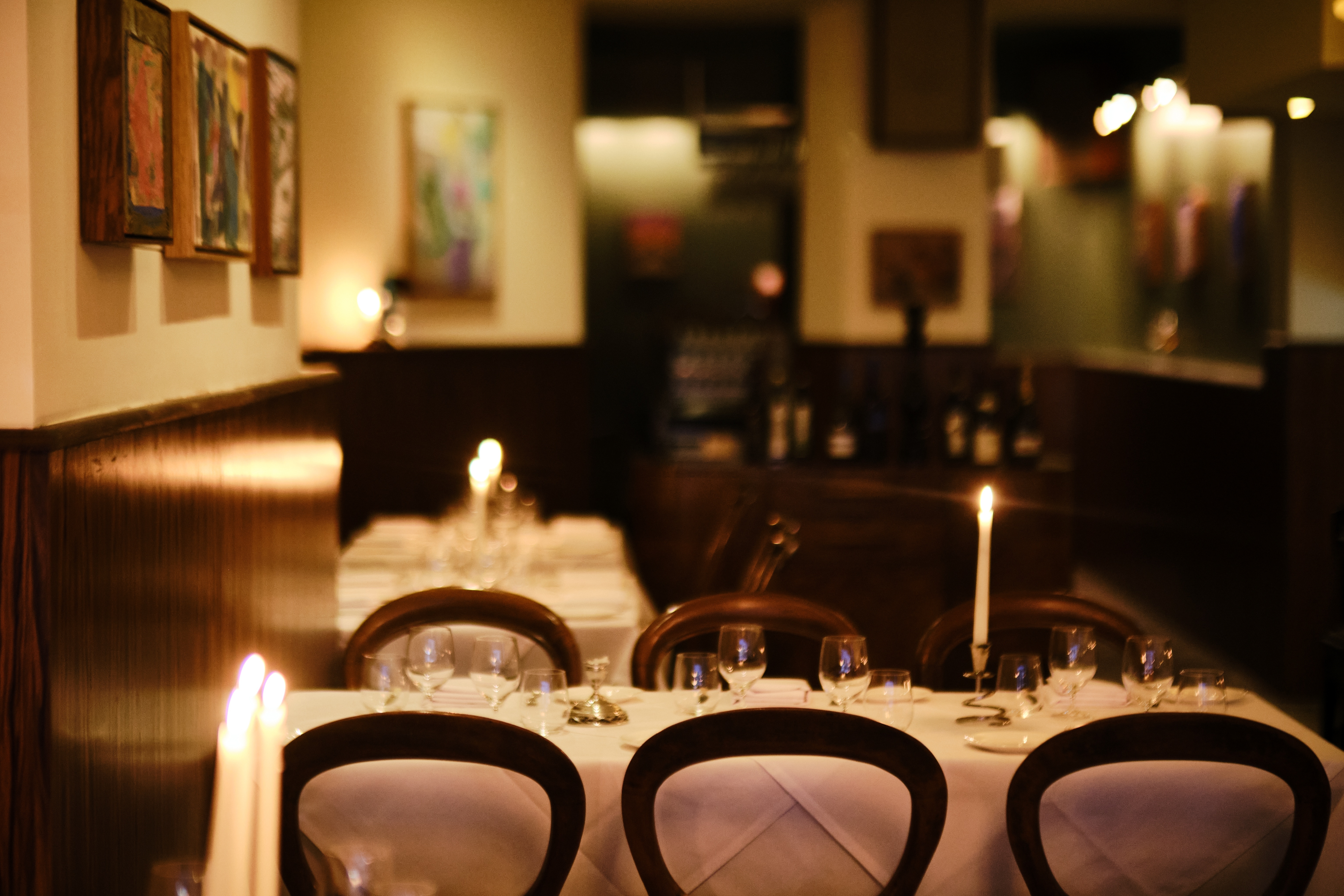 A bistro-style restaurant with wood-paneled walls and wood-framed paintings hanging from the walls.