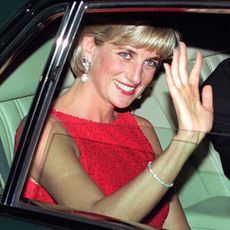 Princess Diana wearing a red dress smiling and waving in a car