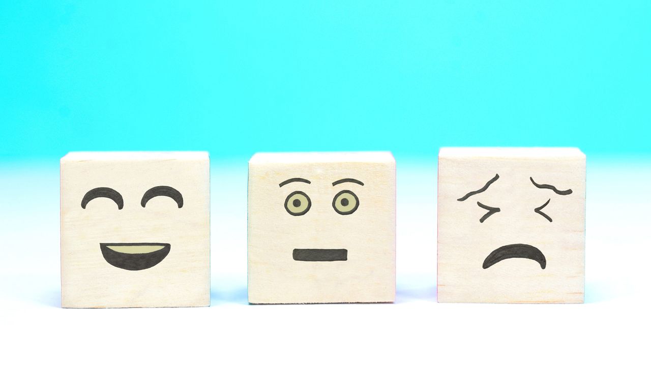 Three blocks with drawn on faces: One smiling, one neutral and one sad.