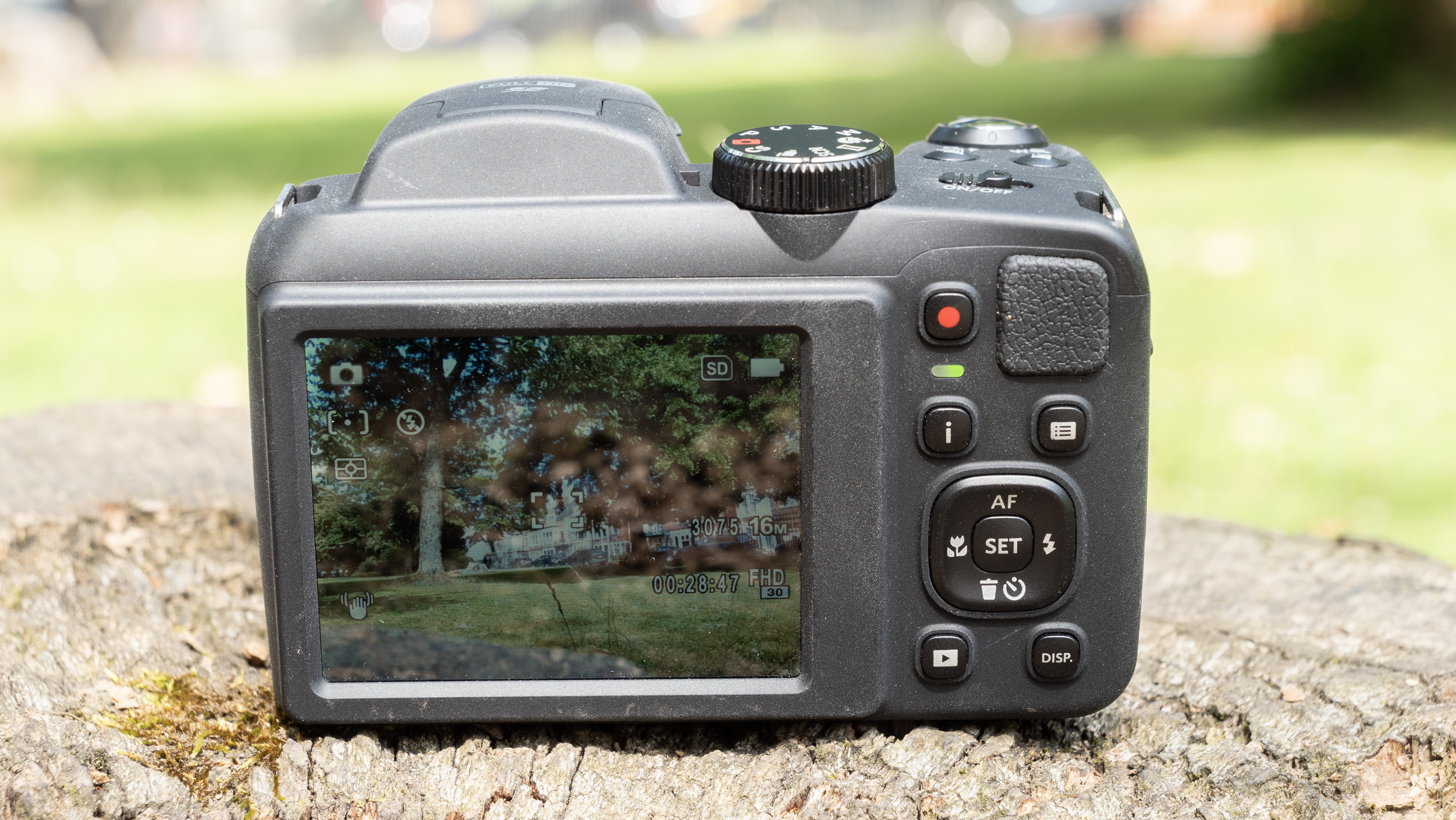 Kodak PixPro AZ255 digital camera in black on a stone surface in front of a green background outside