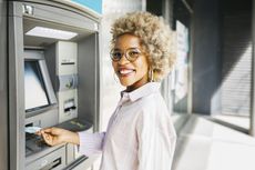 Woman withdrawing money at a cash machine and smiling at the camera