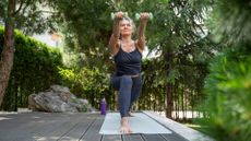 Woman doing Pilates arms workout at home on yoga mat in garden among the trees