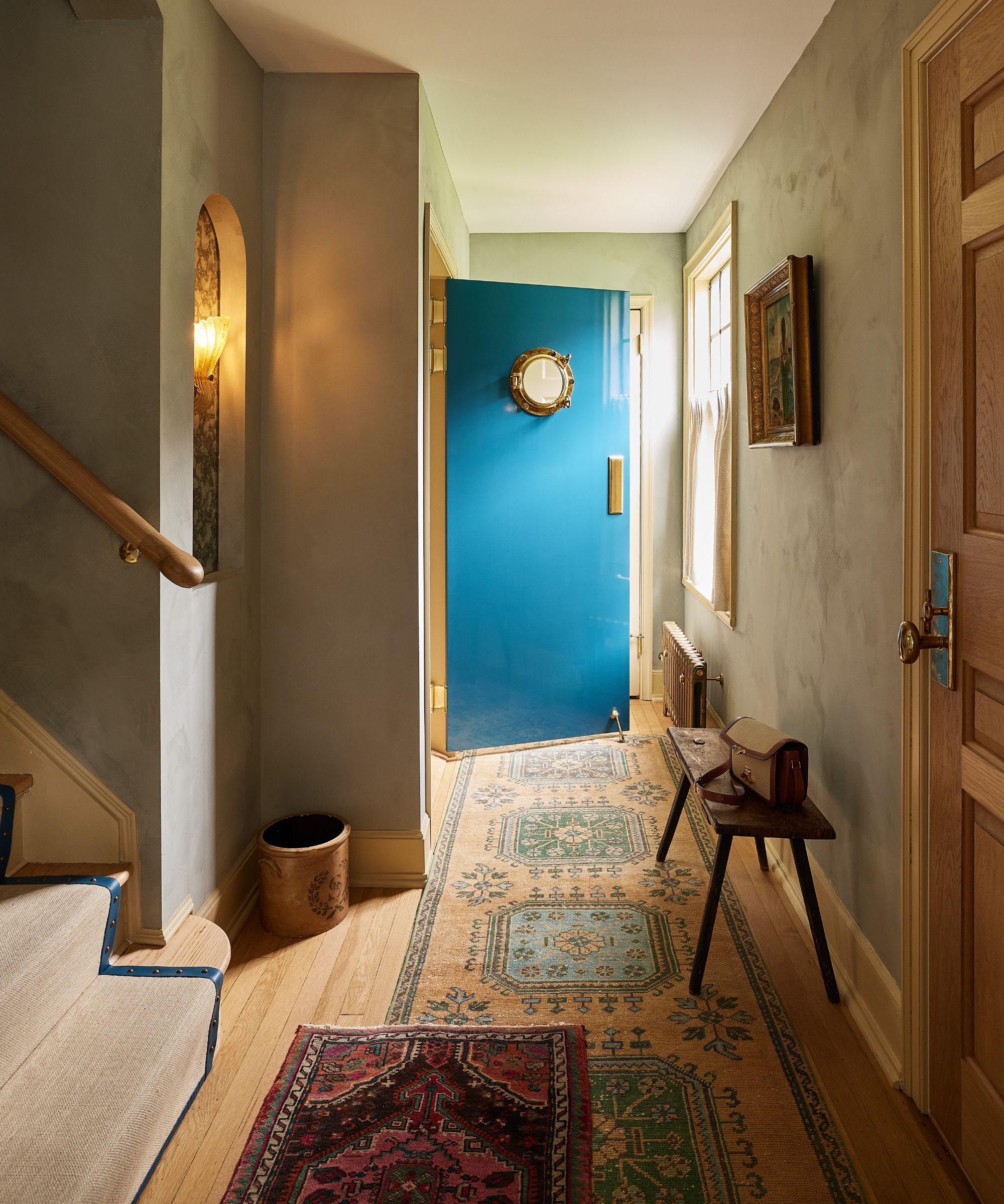 a moody entryway in a New Rochelle home with layered vintage rugs and a gloss blue bathroom door with porthole window