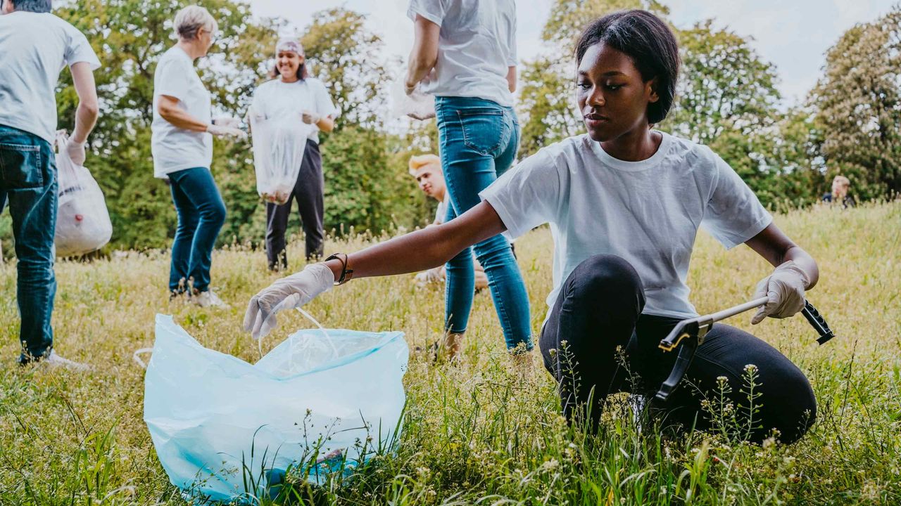 A teen bags trash in a field with other volunteers.