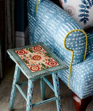 Painted blue stool in the folk style beside blue patterned armchair