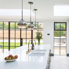 White kitchen with crittal doors leading to a garden and a large white island with a double sink on it