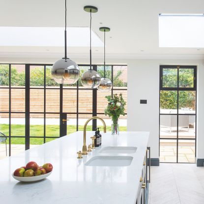 White kitchen with crittal doors leading to a garden and a large white island with a double sink on it