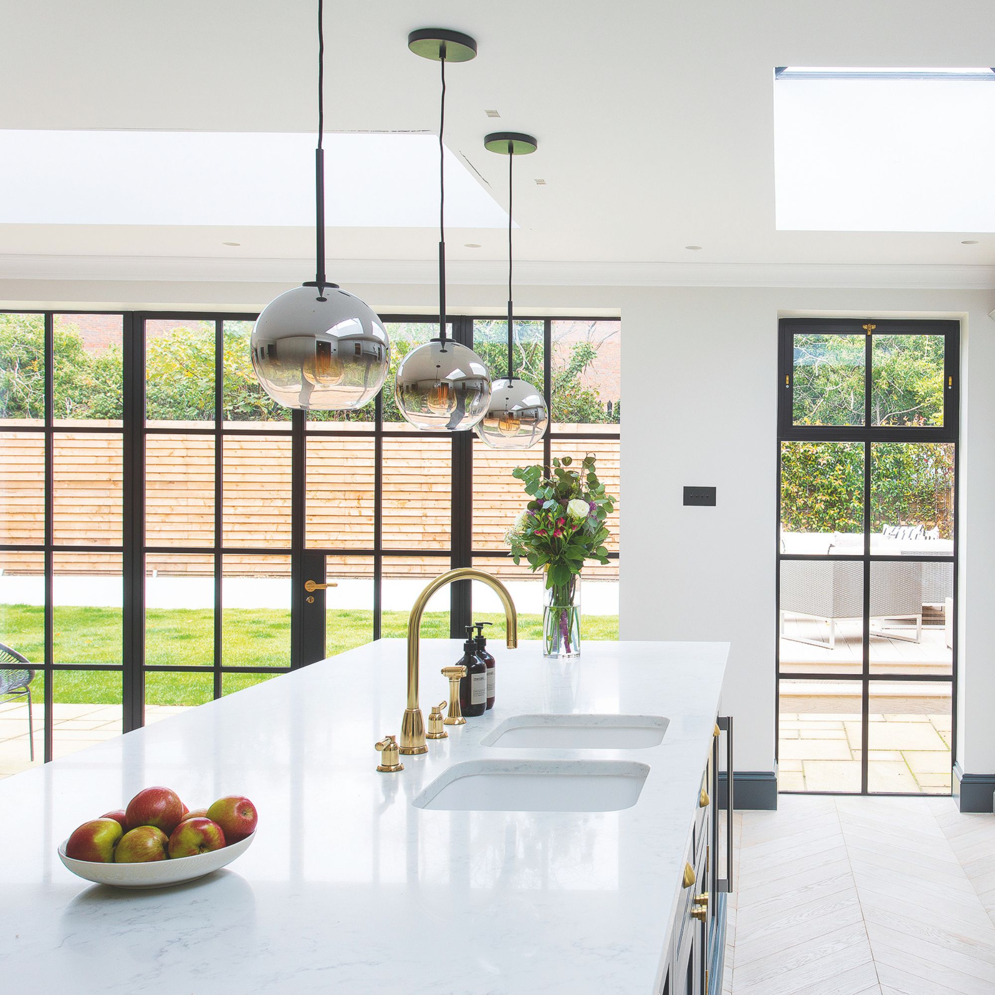White kitchen with crittal doors leading to a garden and a large white island with a double sink on it