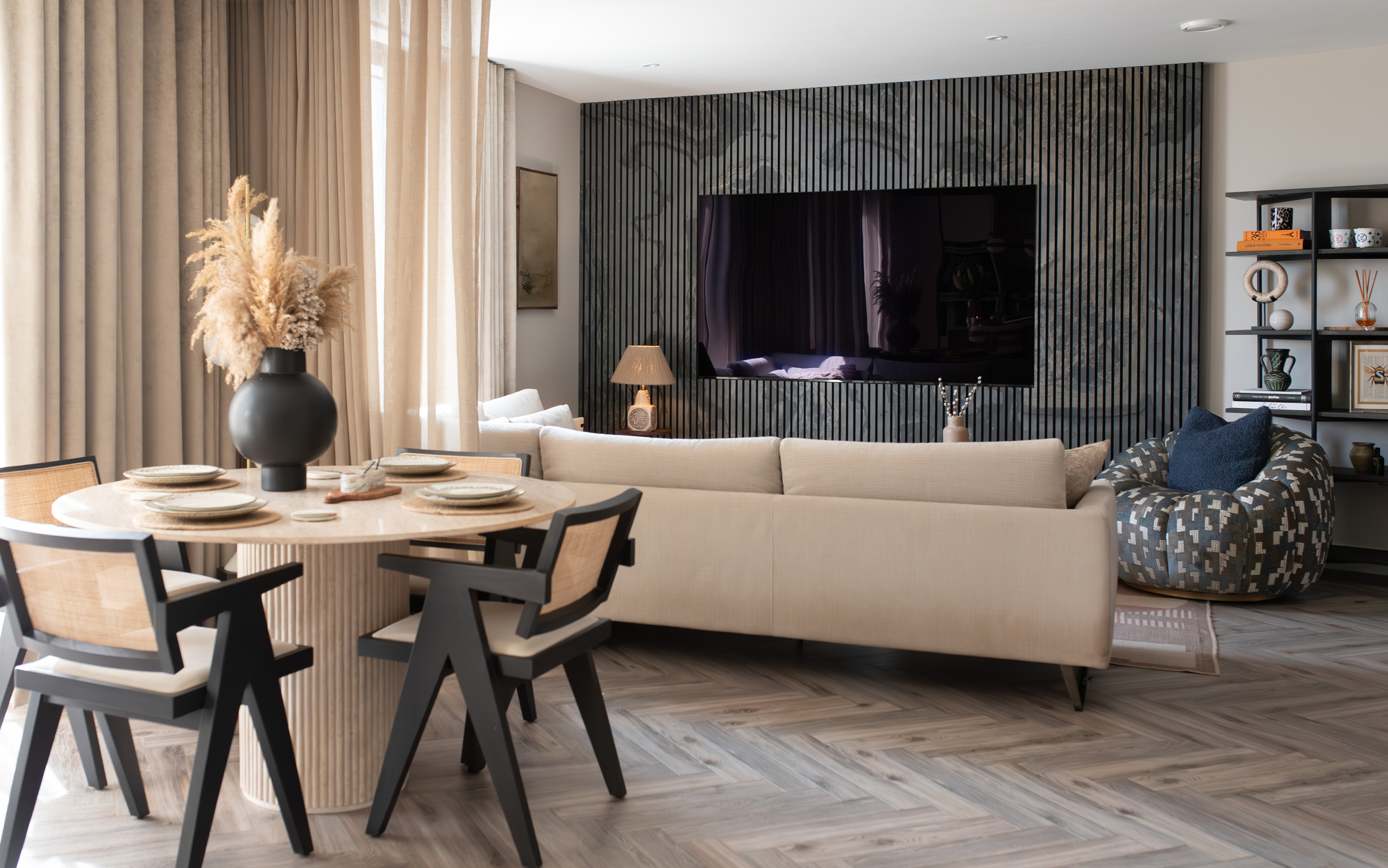 A small open plan living room with a wood slat wall with a large TV built-in, and a circular dining table in the foreground