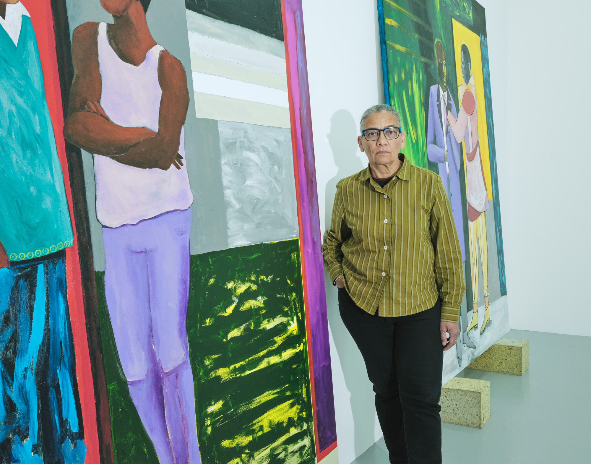 Artist Lubaina Himid standing beside large-scale, colourful artworks of Black figures
