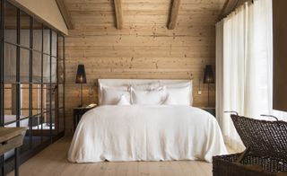 Alternative view of a sleeping area at San Luis featuring a wood panel wall, wooden beams, a bed with white pillows and linen, bedside tables with lamps and a basket