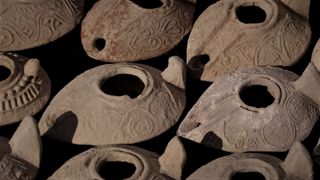 There are nine clay oil lamps. Each is shaped like a teardrop with a hole on top and decorated with circular patterns.