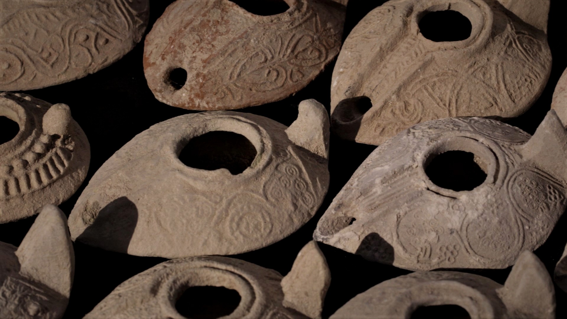 There are nine clay oil lamps. Each is shaped like a teardrop with a hole on top and decorated with circular patterns.