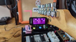 A Peterson Stroboclip HDC clip-on tuner in front of a guitar amp and pedalboard