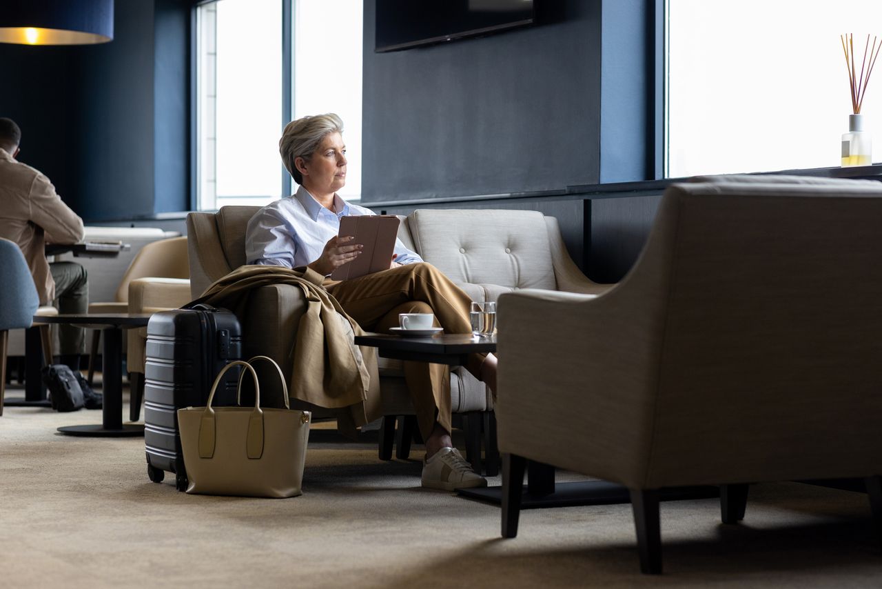 Woman with an ipad looking out the window of an airport lounge. 