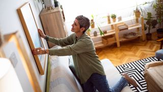 A woman hangs a picture on a wall