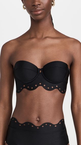 seorang model mengenakan atasan bikini balconette hitam dengan detail lubang tali dan bawahan yang serasi