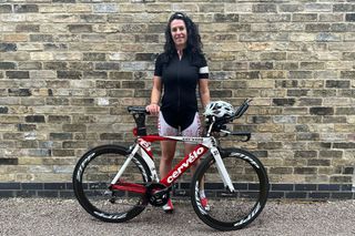 A women in bike kit stands behind her Cervelo time trial bike against a brick wall
