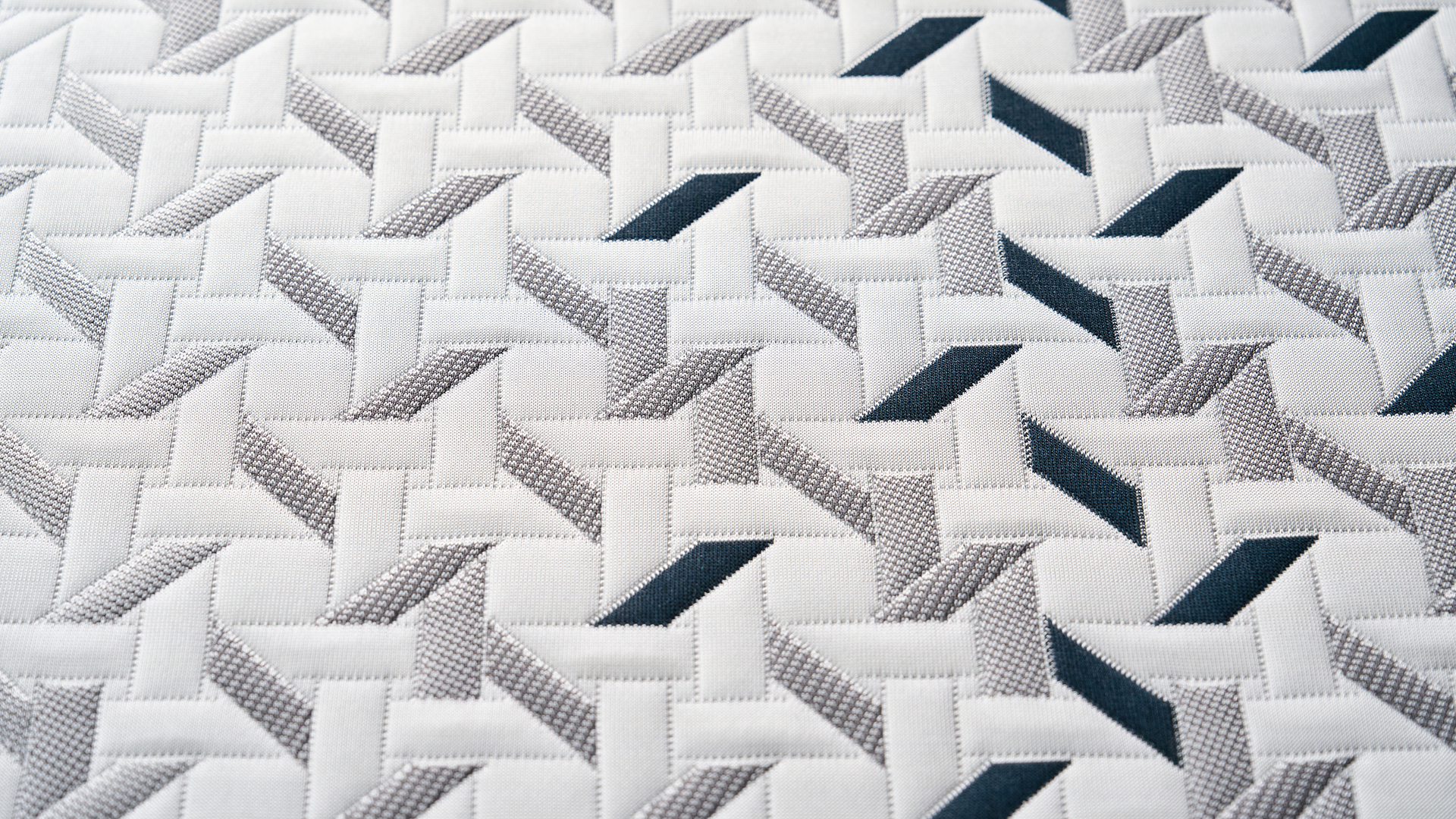 A close-up of the Nectar Ultra Hybrid mattress cooling cover, showing a geometric pattern made up of white, grey and dark blue shapes